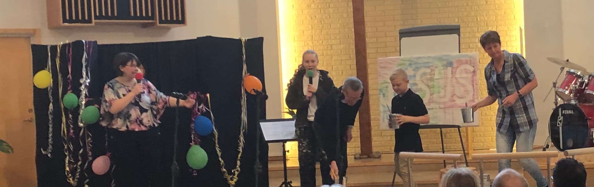 Barn och vuxna med mikrofoner och rekvisita på en scen i kyrkan